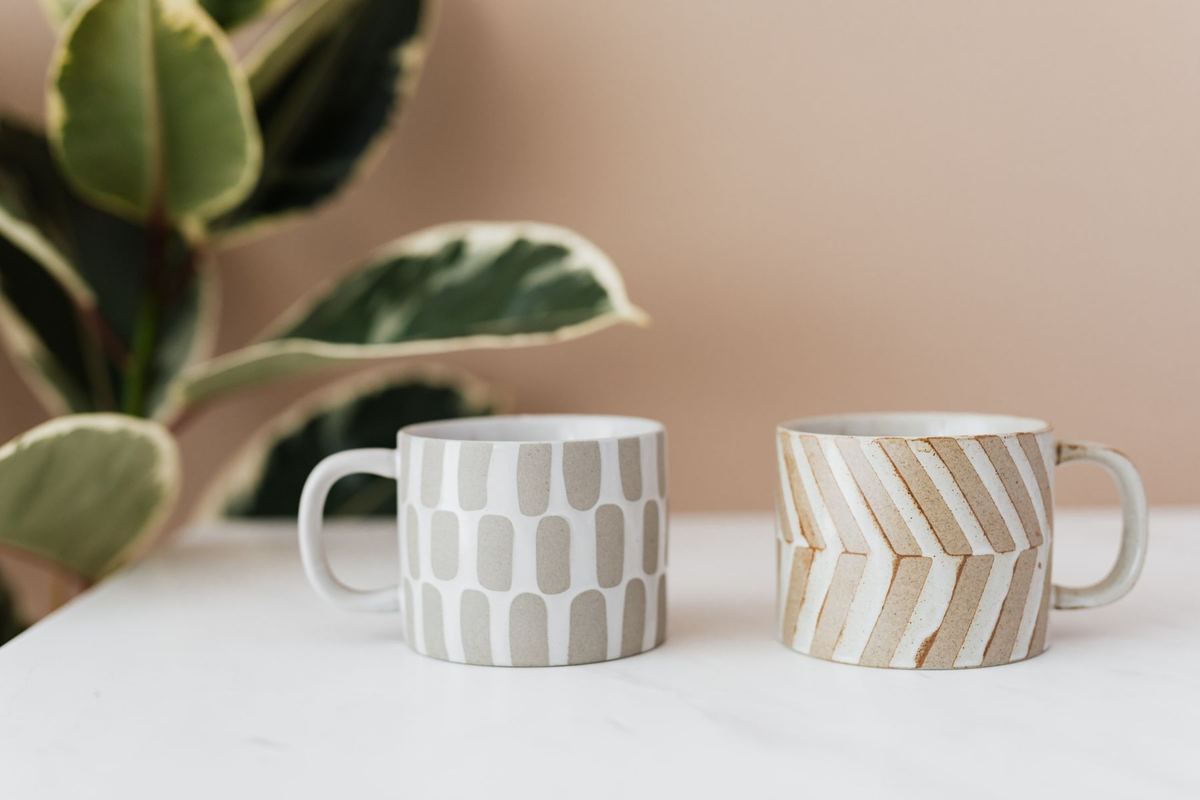 Dos tazas de cerámica con rayas pintadas a mano junto a una planta